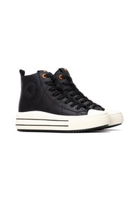 Zapatillas altas de cuero negro con una suela de plataforma blanca, con cordones negros, ojales naranjas y un logotipo circular en el lateral.