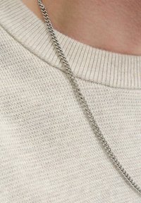 Silberne Kettenhalskette, die über einem hellbeigen, strukturierten Strickpullover drapiert ist, mit kunstvollen Gliedern und einem schlichten Design.