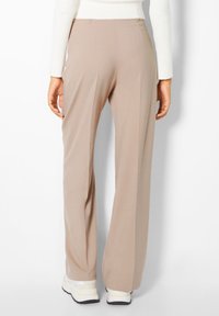 Beige vida byxor gjorda av smidig tyg, med hög midja och avslappnad passform, i kombination med vita och grå sneakers.