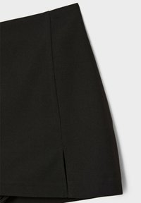 Jupe noire à design structuré, présentant des lignes épurées, des détails de coutures et une petite fente latérale pour faciliter les mouvements.