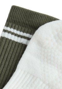 Közelkép egy zöld zokniról, melyen két fehér csík található, mellette egy fehér zokni, talpán tapadós pontokkal.