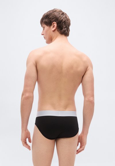Μαύρα εσώρουχα με γκρι ελαστική μέση, κατασκευασμένα από λείο, ελαστικό ύφασμα. Η σχεδίαση διαθέτει εφαρμοστή σιλουέτα και ελάχιστες λεπτομέρειες.