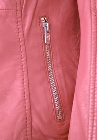 Rosa Lederjacke mit einem metallischen Reißverschluss, sichtbar genäht und mit einer glatten Textur, die das Taschendetail an der Seite hervorhebt.