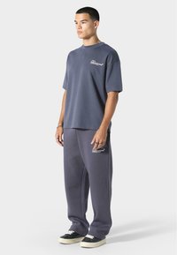 Granatowa bawełniana koszulka typu t-shirt i dopasowane dresy o luźnym kroju, z białym wydrukowanym logo na klatce piersiowej i udzie. Czarne sneakersy.