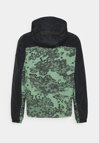 Grön och svart huva jacka med ett kamouflage mönster, texturerad tyg, elastiska ärmar och en slät svart ovandel.