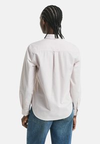 Person with braided hair wearing a light striped long-sleeve shirt and blue jeans, shown from behind against a plain background.