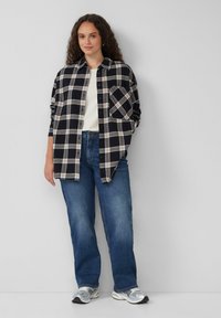 Schwarzes Flanellhemd mit weißem und grauem Karomuster, Knopfverschluss vorne, eine Brusttasche, kombiniert mit blauen Jeans und sportlichen Schuhen.