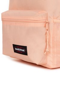 Pudrowy plecak Eastpak w kolorze brzoskwiniowym z zamykaną na zamek przednią kieszenią, teksturowanym korpusem oraz czarną łatą z logo przedstawiającą glob.