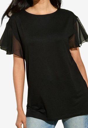 T-shirt noir avec manches courtes transparentes et à volants. Encolure arrondie et texture douce et lisse. Associé à un denim bleu clair.