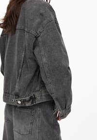 Chaqueta de mezclilla gris de gran tamaño con un acabado lavable, costuras definidas y detalles de puños abotonados. Presenta bolsillos frontales y un dobladillo recortado.