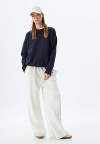 Sudadera navy con hombros caídos, pantalones blancos de pierna ancha y una gorra clara. La sudadera tiene puños de canalé; tejido texturizado y suave.