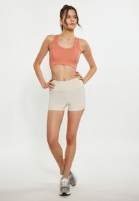 Ferskenfarvet sportstop og beige shorts. Sportstoppen har en tætsiddende design og brede stropper. Shortsene er glatte med en elastisk talje og en tætsiddende pasform.