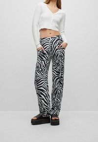 Weiße, kurz geschnittene Strickjacke mit Knöpfen, kombiniert mit weit geschnittenen, schwarz-weißen Zebra-Muster-Hosen. Dazu gehören flache Plateau-Sandalen.