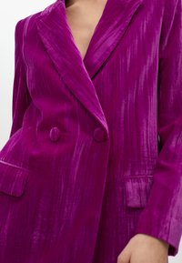 Dubbelknäppt kavaj i ljus magenta sammet. Har slagkragar, texturerad yta och två framfickor. Slät, glansig yta.