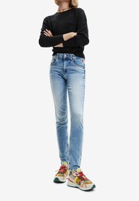 Svart texturerad tröja, blå slim fit-jeans och flerfärgade sneakers med nätöverdel, snörning och dämpad sula.