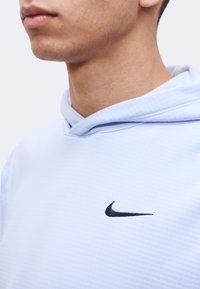 Κοντινό πλάνο ενός ατόμου που φοράει γαλάζιο φούτερ Nike με μαύρο λογότυπο swoosh στο στήθος, δείχνοντας το κάτω μισό του προσώπου και τον λαιμό.