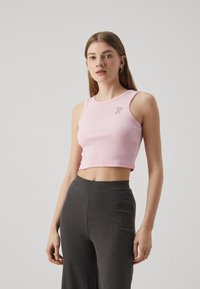 Svetloružový rebrovaný crop top s okrúhlym výstrihom a malým logom "B" zdobeným kryštálmi, v kombinácii s tmavosivými rebrovanými nohavicami.