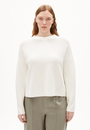 Weißer, strukturierter Pullover mit rundem Halsausschnitt, überschnittenen Schultern und langen Ärmeln, kombiniert mit hellgrünen, taillierten Hosen.