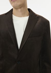 Bruine suedew blazer met een enkele knoopsluiting, notch lapels en een borstzak, gelaagd over een witte crewneck shirt.