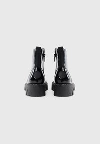 Black patent leather ankle boots with a chunky black rubber sole and side zippers. Features elastic accents on the sides for easy wear.