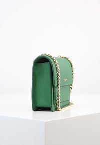Borsa a tracolla in pelle verde con catena dorata, forma rettangolare, superficie testurizzata, chiusura a pattina e dettaglio del logo impresso nella parte anteriore.