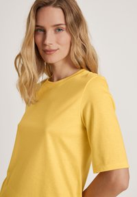 Geel kort mouwen top van zachte stof met een ronde halslijn en een relaxte pasvorm, met een zachte textuur en minimale details.