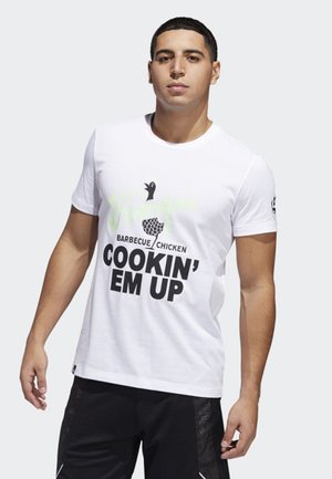 Camiseta de algodón blanca con un gráfico en negro y verde que dice “Barbacoa de Pollo Cocinándolos” y un icono de ave, con escote redondo.