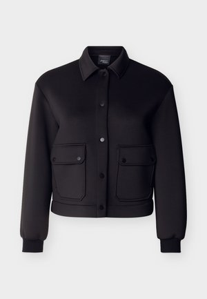 Fekete hosszú ujjú dzseki gallérral, elöl patentos gombokkal és két fedeles zsebbel patentos záródással a deréknál.