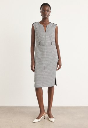 Black and white checked midi dress with a V-neck, cap sleeves, side slit, and a belted waist detail. Model pairs it with white heels.
