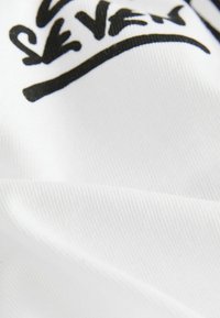 Tessuto bianco con una texture liscia, caratterizzato da un design grafico nero. Il design include lettering stilizzati e accenti curvi.