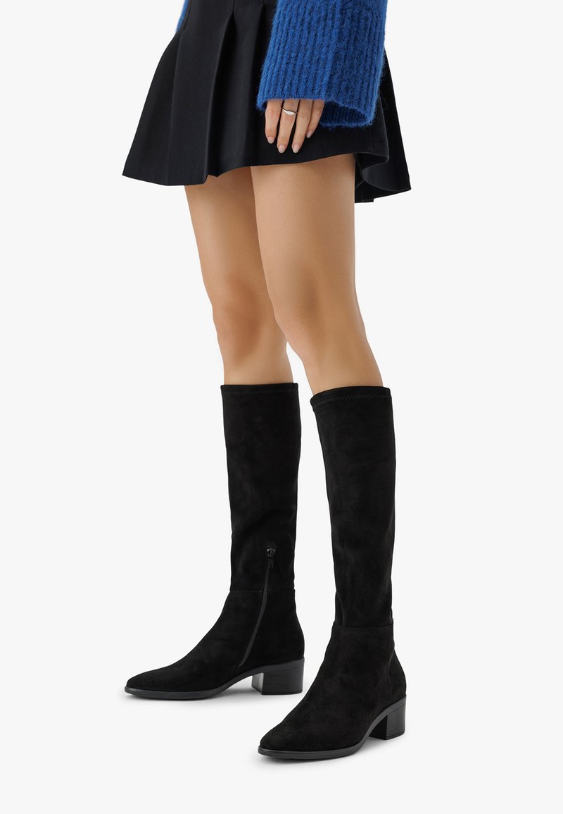 Black suede knee-high boots with a square toe and block heel. Side zip closure. Styled with a pleated black skirt and blue knit sweater.