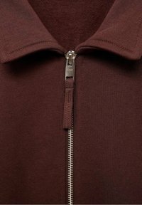 Pull brun à fermeture éclair avec une texture côtelée, doté d'un col classique et d'un détail de fermeture éclair argentée à l'avant.