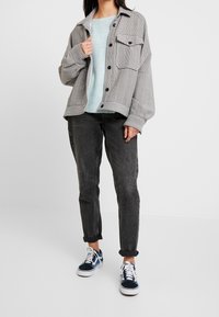 Giacca a quadri grigia oversize, maglione blu a trama, jeans neri e sneakers navy e bianche. Presenta tasche grandi e chiusura a bottoni.