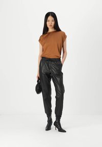 Brown short-sleeve top, wide neckline, paired with black leather joggers featuring an elastic waistband and tapered cuffs, complemented by heeled ankle boots.
