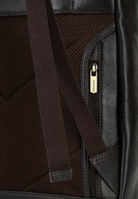 Tmavě hnědá texturovaná kůže a síťovina se zipovou kapsou. Hnědý popruh a kontrastní prošívání jsou viditelné.