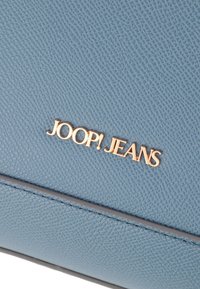 Modra teksturirana usnjena torba z zlatim logotipom "JOOP! JEANS". Površina prikazuje subtilen vzorec in šivane detajle ob robovih.