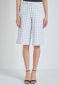 Pantalones cortos a cuadros blancos con un patrón de cuadrícula en color marino, con pliegues en la parte delantera y bolsillos laterales. Corte ajustado, que termina justo por encima de la rodilla.