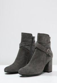 Graue Wildleder-Ankle-Boots mit spitzem Vorderteil, seitlichem Reißverschluss und dekorativem Riemen mit silberner Schnalle. Klobiger, hoher Absatz.