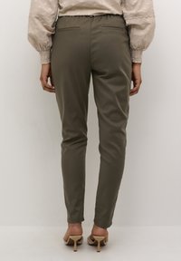 Pantalons ajustés vert olive avec une texture lisse, taille élastique et deux poches arrière, associés à des talons ouverts neutres.