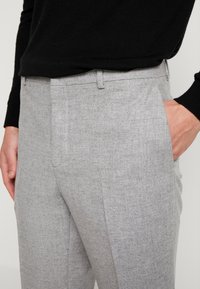 Lichtgrijze broek van een gestructureerde stof, met een vlakke voorkant, zijzakken en een getailleerde pasvorm.