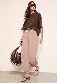 Pruun kootud lühikeste varrukatega top, liivakarva laia säärega püksid mansetiga, pruun vöö metallist pandlaga, pruuni äärisega käekott, kontsaga sandaalid.