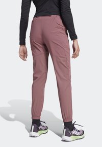 Taperade, elastiska midje-joggers i ljusrosa tyg, med sömdekorationer och en mjuk textur. Matchat med mörka träningsskor.