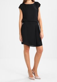 Vestido negro de manga corta con escote redondeado y detalle drapeado en la cintura. Tejido suave y corte por encima de la rodilla.