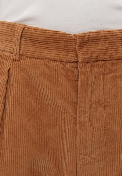 Brune cordfløyelsbukser med vertikale ribber, med midjebånd og frontfolder, med en myk, teksturert overflate.
