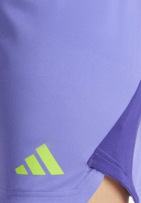 Paarse sportshorts met een gladde textuur, met een groen logo en accent aan de linkerkant. Het ontwerp omvat zijsplitten voor meer bewegingsvrijheid.
