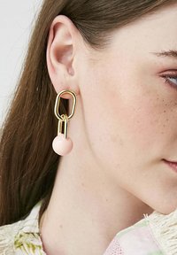 Zlato-tonirane uhane, ki se ponašajo z abstraktno geometrijsko zasnovo in svetlo rožnatimi, okroglimi biseri na dnu.