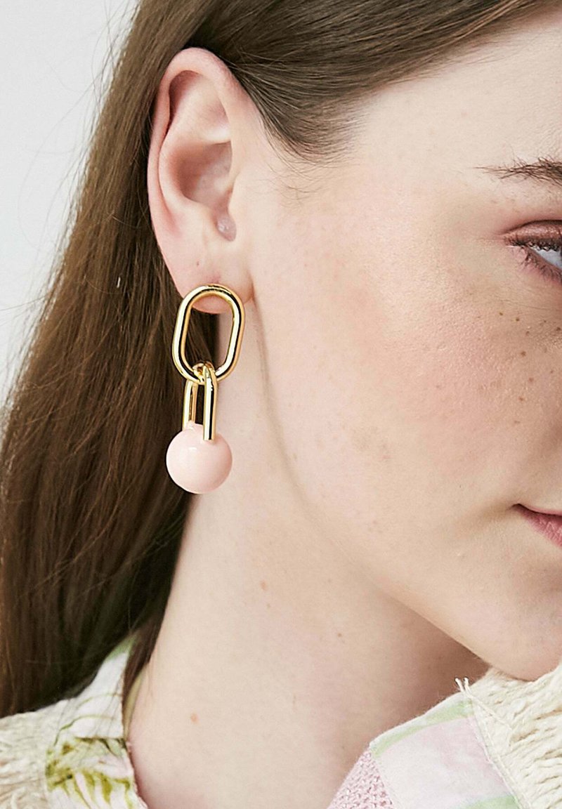 Zlato-tonirane uhane, ki se ponašajo z abstraktno geometrijsko zasnovo in svetlo rožnatimi, okroglimi biseri na dnu.