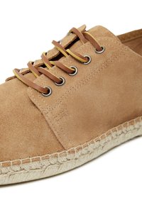 Semišové hnědé boty se skládají z plochého designu, mají hnědé šněrování skrze kovové očka a pro kontrast a texturu jsou doplněny tkaným juteovým středním podešvem.