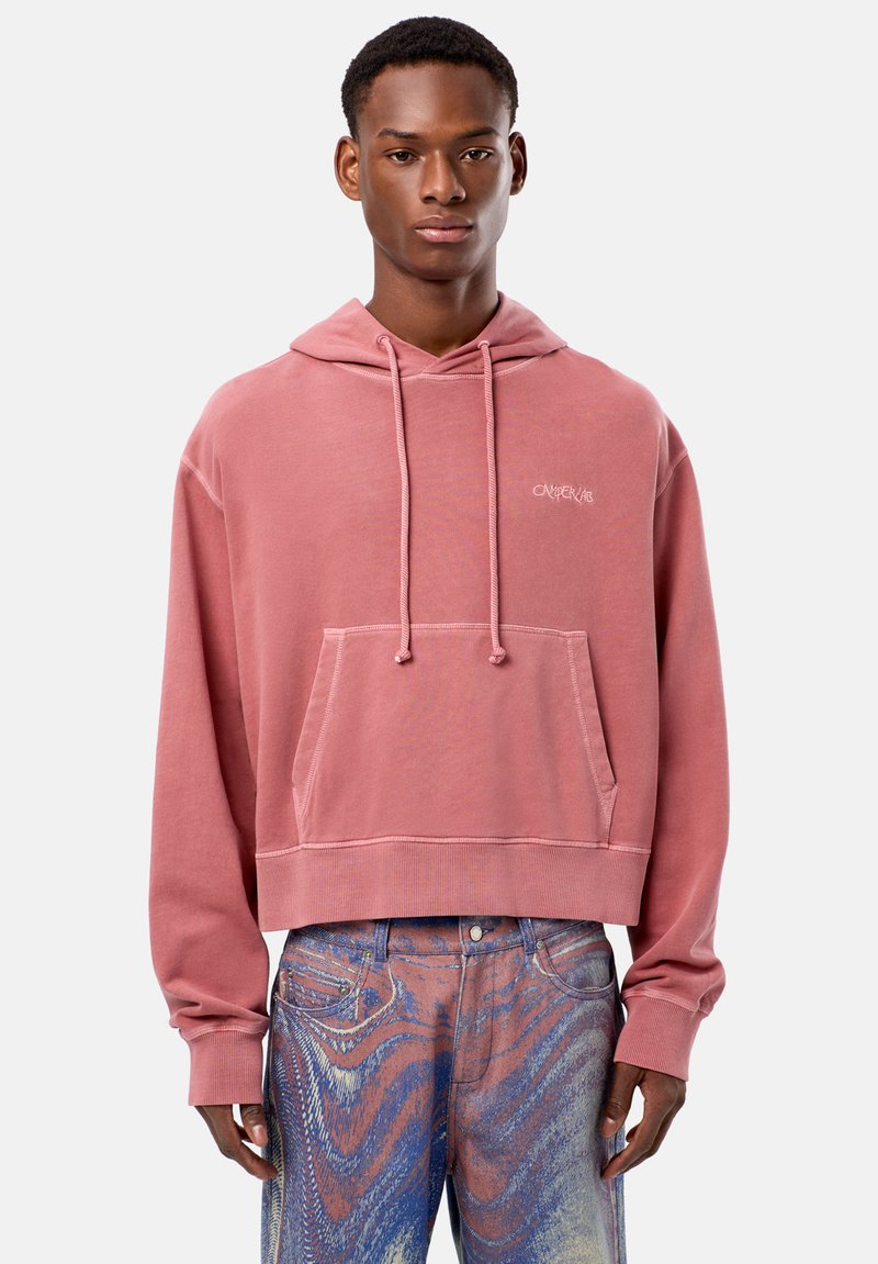 Beskurven rosa huvtröja med en framficka, justerbara snoddar och broderad logotyp på bröstet, i kombination med mönstrade blå jeans.