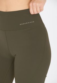 Olijfgroene high-waisted legging van glad, rekbaar materiaal, met gestikte accenten en het "ENDURANCE" logo.